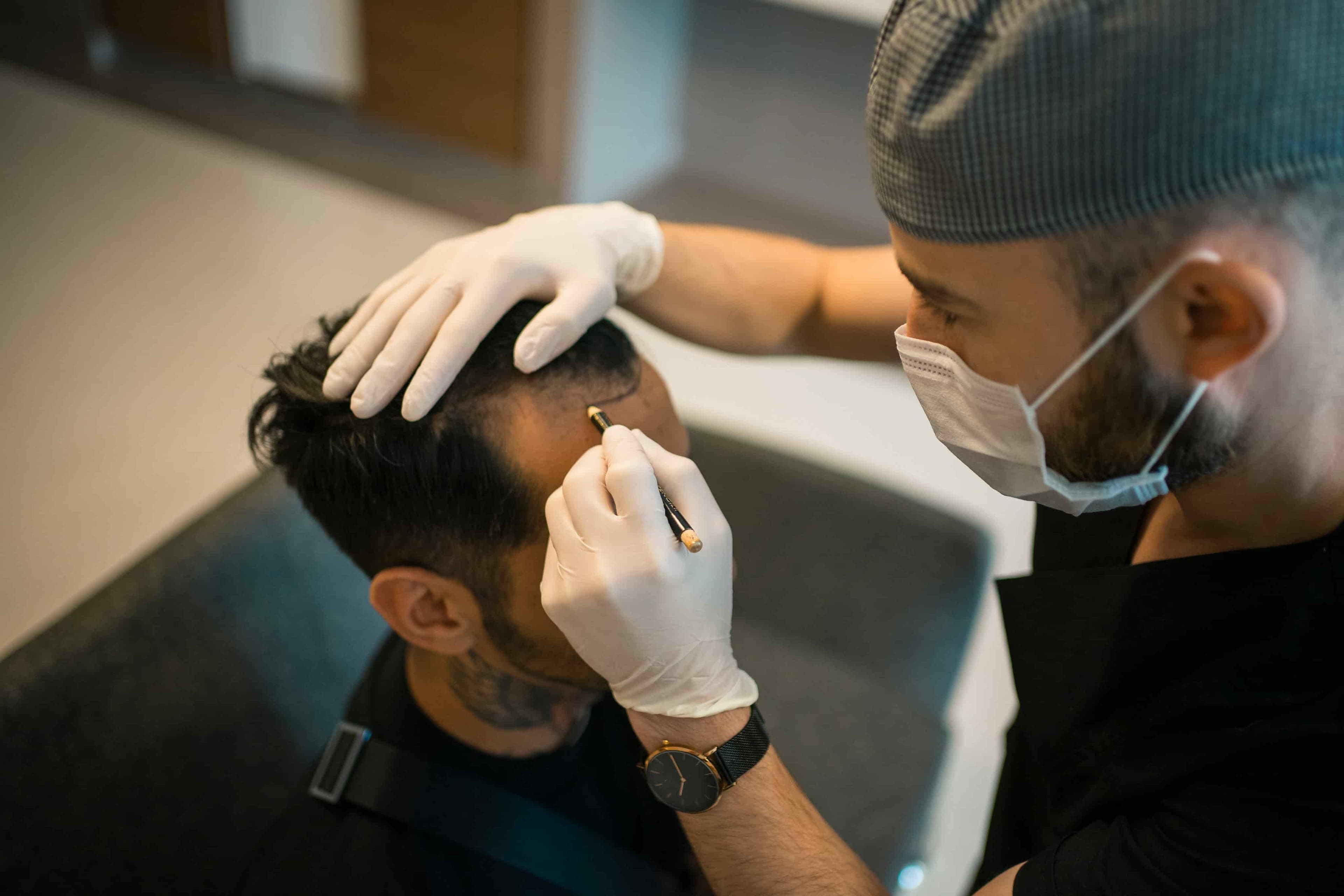 A surgeon is drawing a hairline on a patient's head.