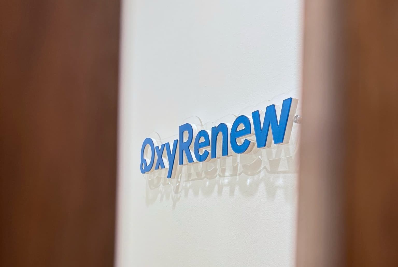 The OxyRenew logo, mounted on a wall, as seen between two wooden slats.