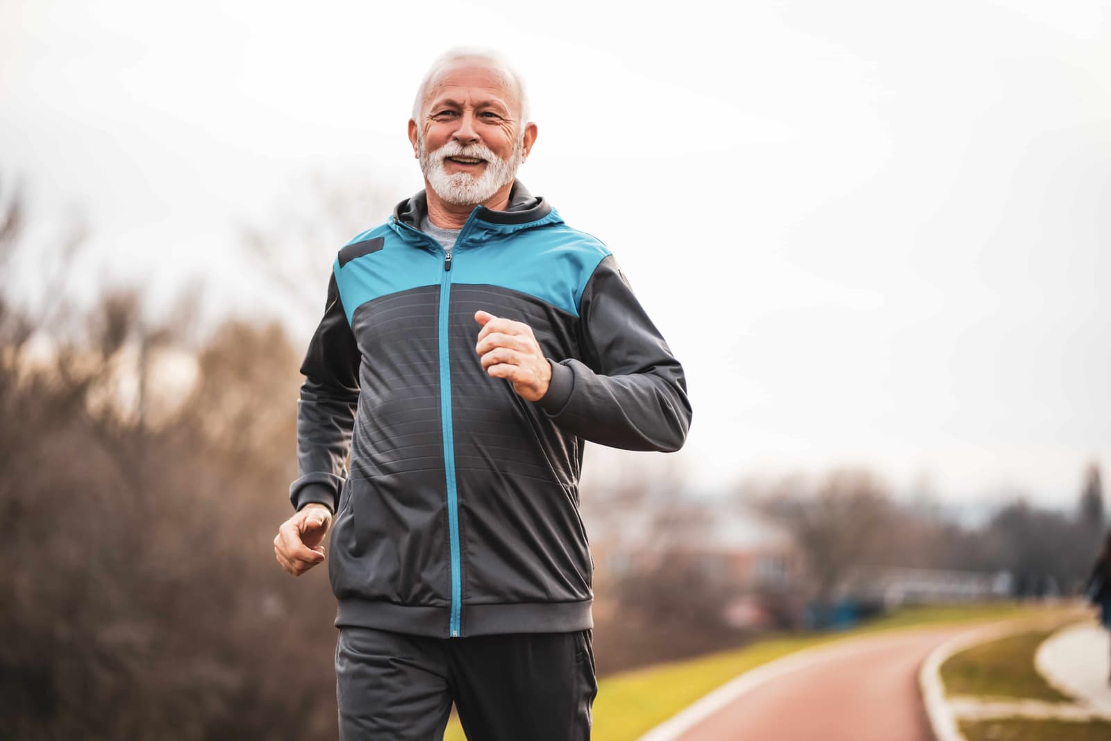 An older gentleman is jogging through a park.