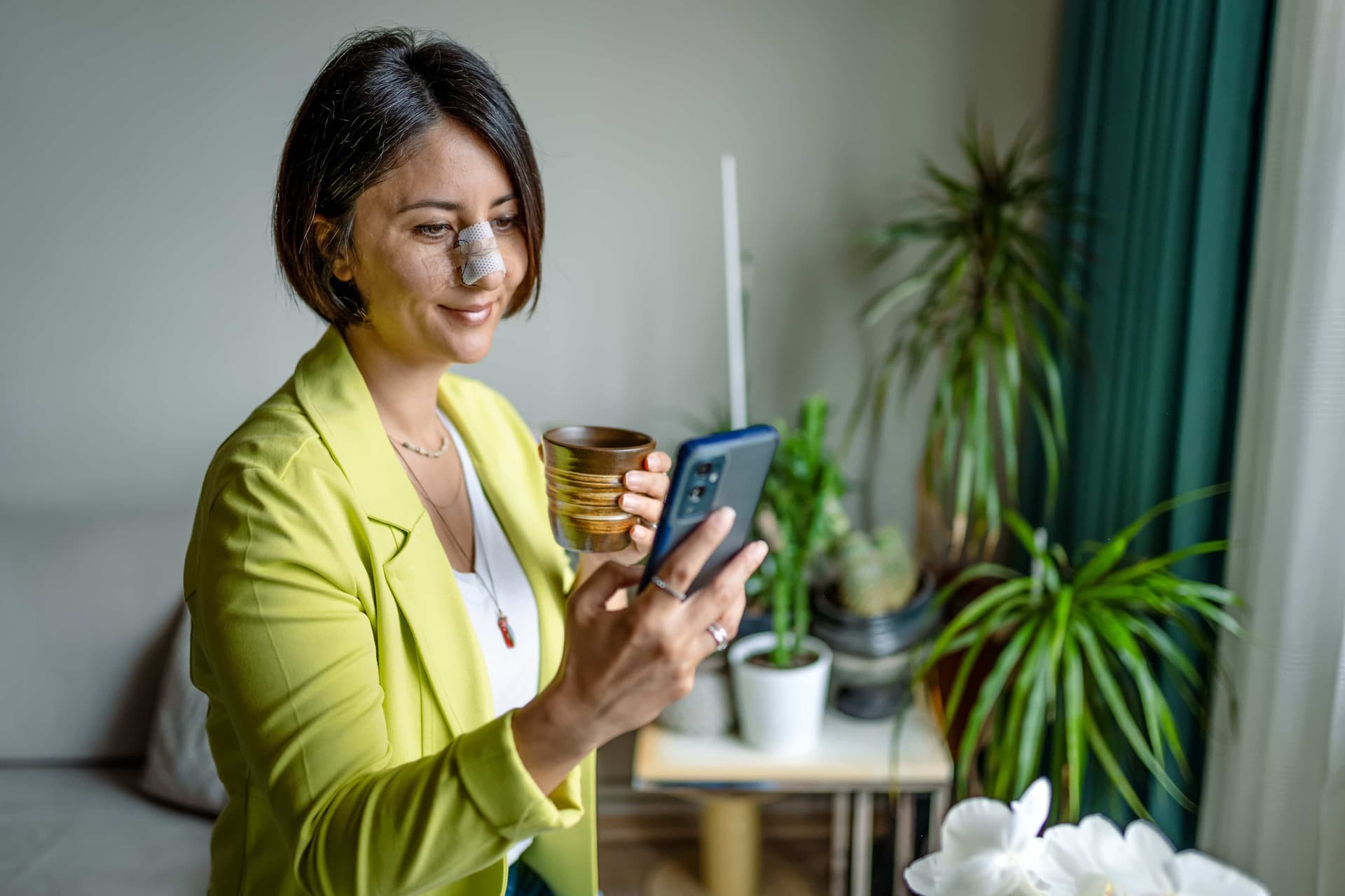 A woman is using her phone while recovering from rhinoplasty.