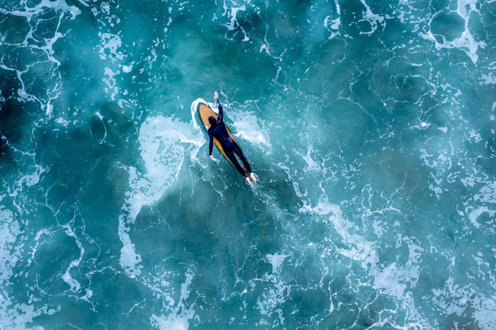 A bird's eye view of a surfer paddling on a surfboard.