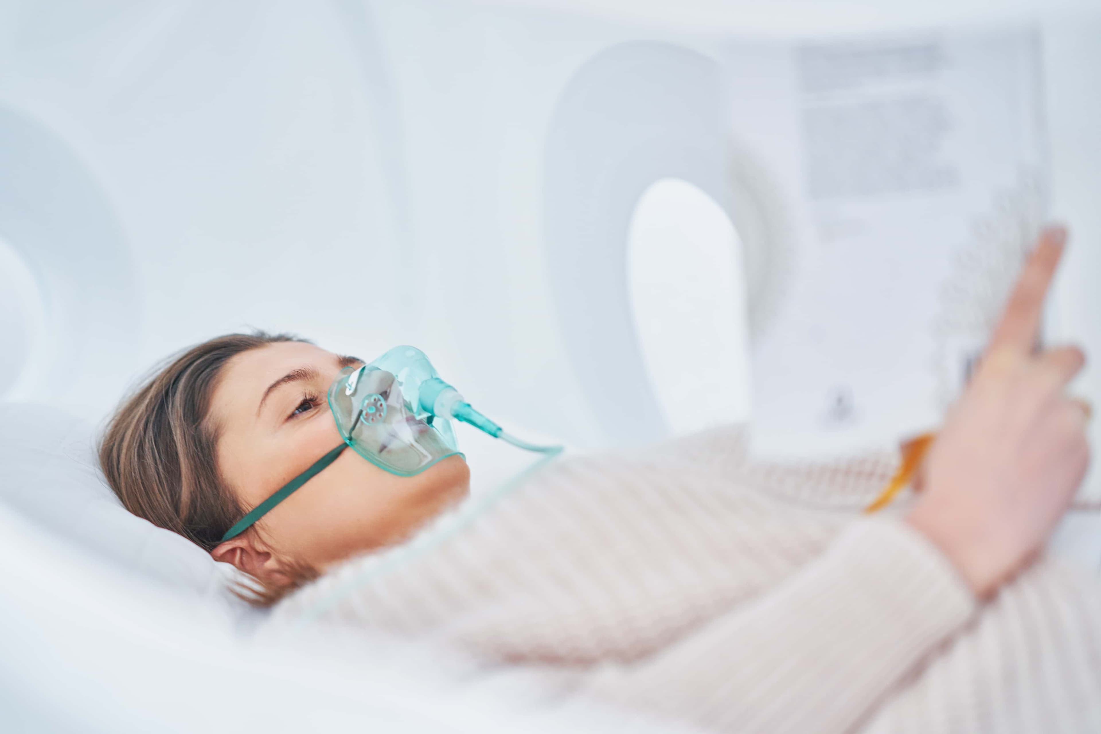 A woman is reading a book while lying in a hyperbaric oxygen chamber.