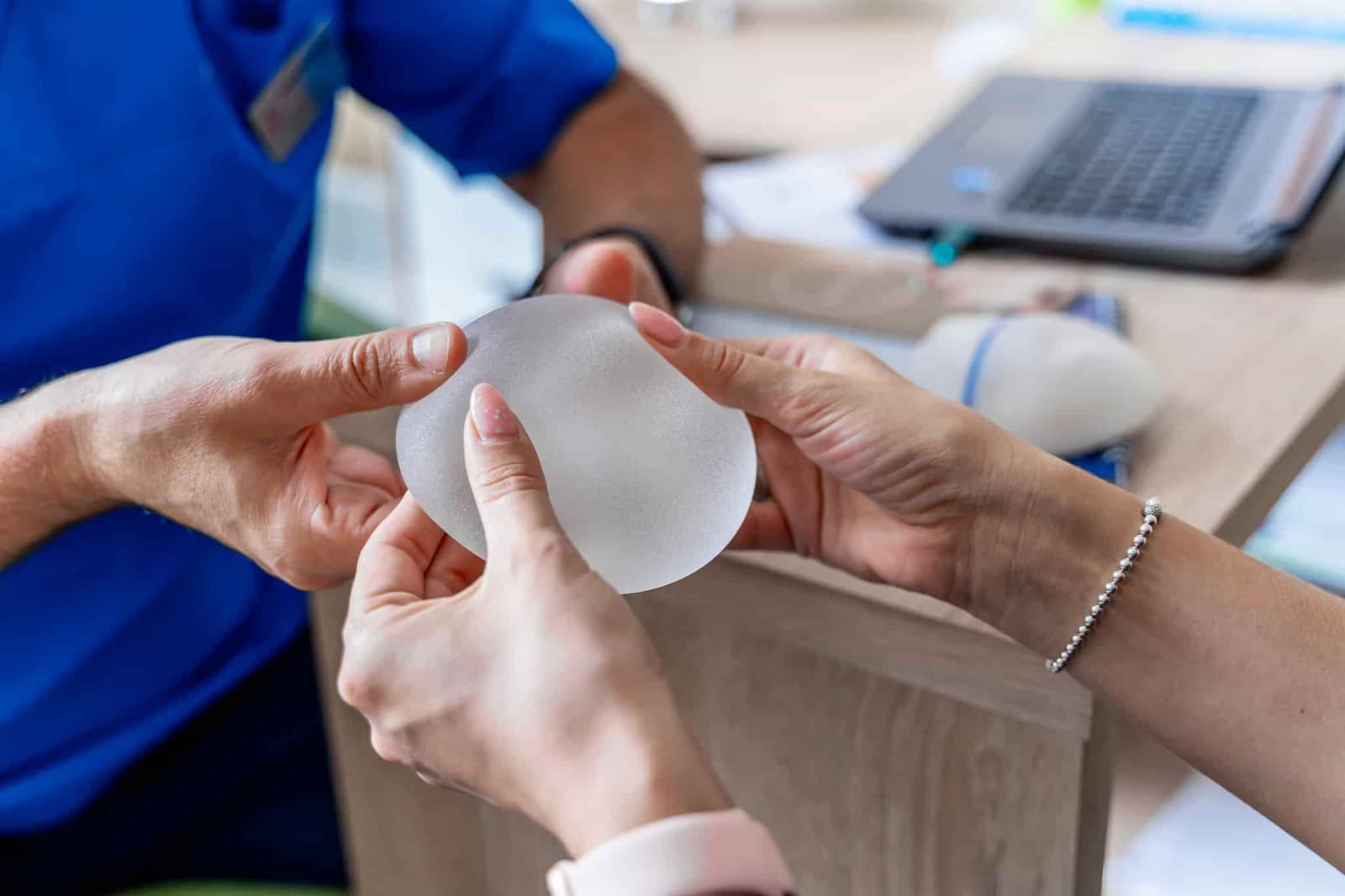 A patient holding a silicone breast implant during a consultation with her plastic surgeon.